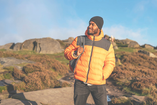 Portrait of happy handsome man tourist with backpack hiking and enjoying mountains landscape at sunset in England. A trip to the mountains with a backpack. Enjoy hiking and exploring new places concept toned image