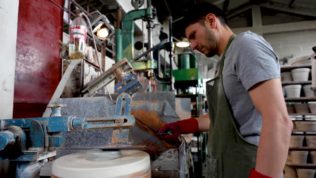Latin American male potter preparing a piece of clay hydrating and shaping it to pass it to another machine