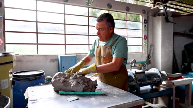 Focused man slightly kneading the clay before putting it through a machine to remove all the air at a pottery factory