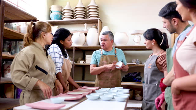 Group of Latin American people in a pottery class listening to the teacher while explaining something about a piece