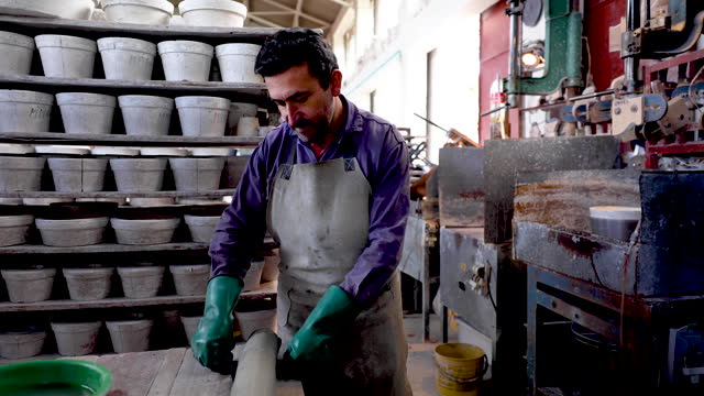 Mature artisan slicing a piece of clay and putting it on machine to make a bowl at a pottery factory