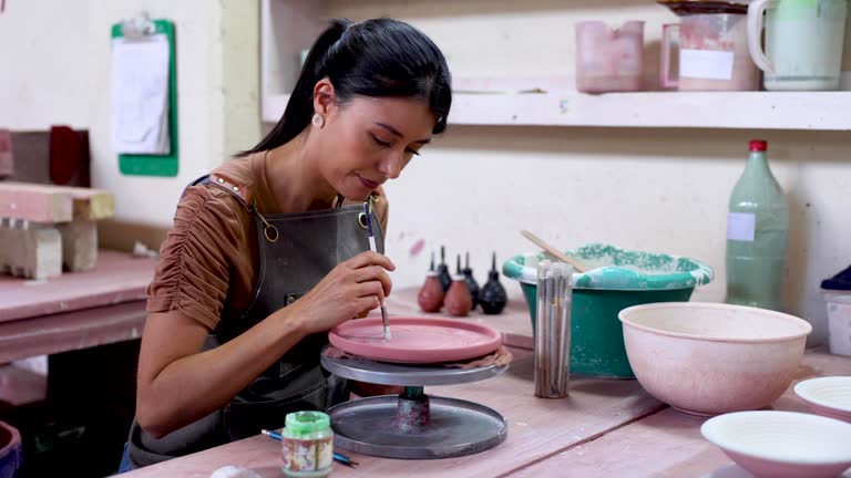 Beautiful female potter painting a plate with enamel on a wheel at a pottery factory