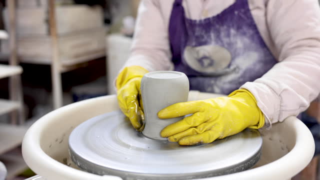 Unrecognizable person carving a mug on a pottery wheel at the factory
