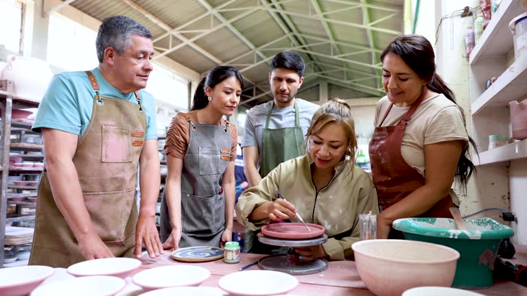 Cheerful woman teaching a diverse group in age how to paint with enamel a plate at a pottery factory