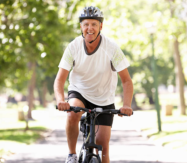 homme d'âge mûr vélo au parc - cycling senior adult sports helmet men photos et images de collection