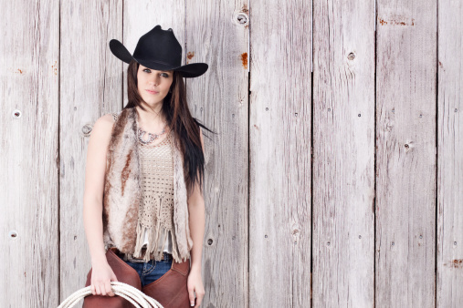 Beautiful young cowgirl with a gun sitting on cowboy cart