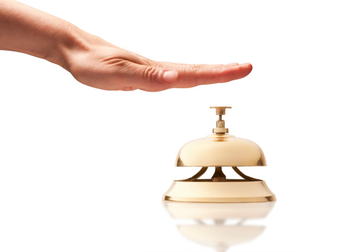 Hand ringing brass bell on hotel reception desk