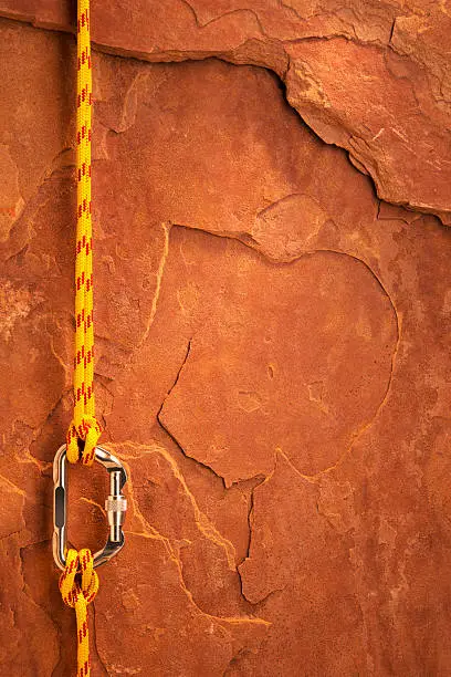 This is a photo taken in the studio of yellow climbing rope attached to a carabiner with a clove hitch knot on each end in front of a sheet of red rock.Click on the links below to view lightboxes.