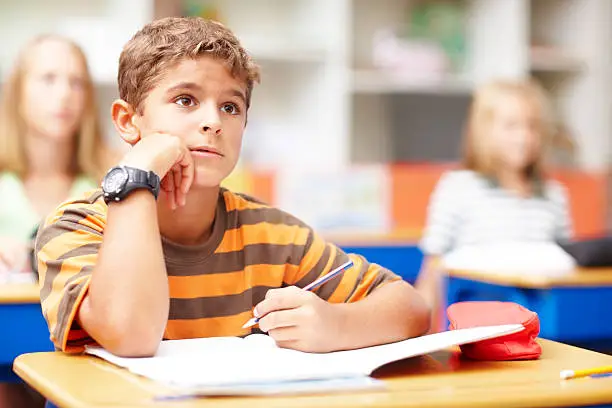 Young boy in class listening to his teacher while taking notes - copyspace