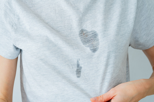 Unrecognized surprised female showing at dirty grease stain on a gray t-shirt. Daily life stain concept