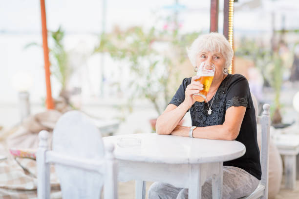istock Mature woman sitting at a table in a summer cafe and drinking beer 1754523005