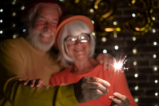 Blurred caucasian senior couple holding sparklers celebrating new year. Happy lifestyle for mature retirees, party lights