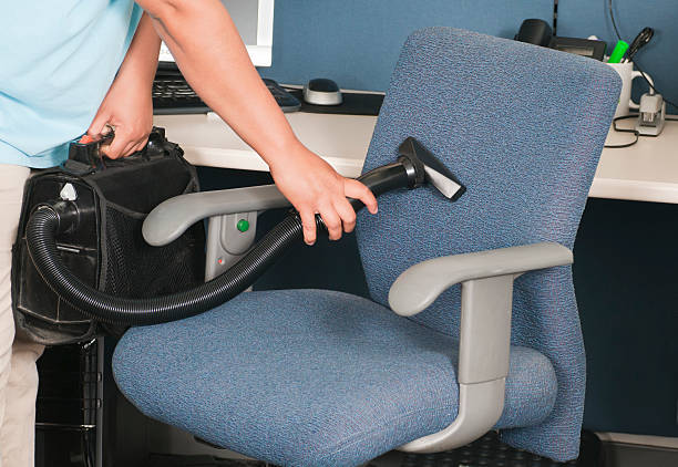Close up of the arms of a woman from a professional cleaning service vacuuming a chair in an office.