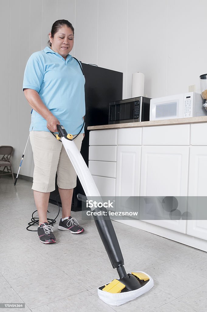 Woman Cleaning a Corporate Break Room Hispanic woman from a professional cleaning service cleaning the floor of a corporate kitchen or break room.Click below for more commercial cleaning images: Adult Stock Photo