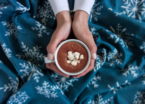 woman a cup of hot chocolate with marshmallows on a wool blanket