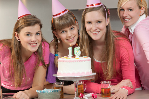 Young excited teen girl wearing birthday hat, holding balloon and plate with cake, feeling happy and satisfied with surprise, isolated on pink background