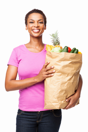 Portrait of a smiling African American woman holding a bag of healthy groceries. Vertical shot. Isolated on white.