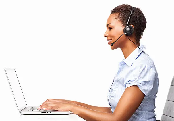 Side view of a smiling African American female IT operator typing on her laptop. Horizontal shot. Isolated on white.