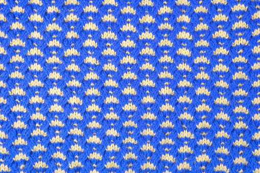 Knitted blue and yellow abstract background. Large knitted fabric with a pattern. Close-up of a knitted blanket. Copy space