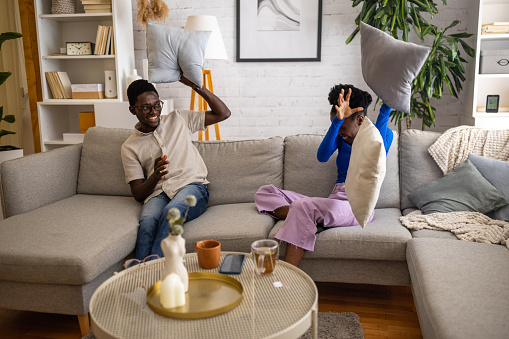 Two people, young black couple having fun playing pillow fight on sofa at home.