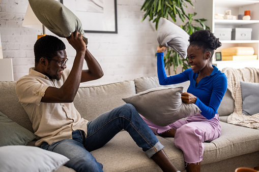 Two people, young black couple having fun playing pillow fight on sofa at home.
