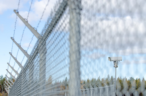 Surveillance camera at the airport surrounded by metallic fence and barbwire during autumn day