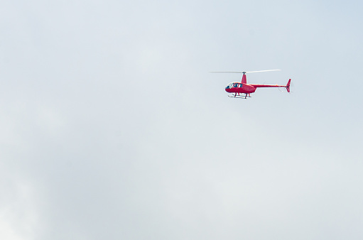 Small red helicopter flying during autumn day.