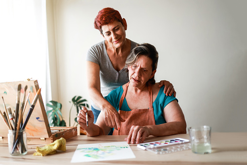Gay senior couple painting with watercolor on canvas at art workshop - LGBTQ Lesbian family having fun together at home