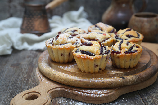 Plum muffins, cezve and cup of coffee, powdered sugar dressing on wooden background