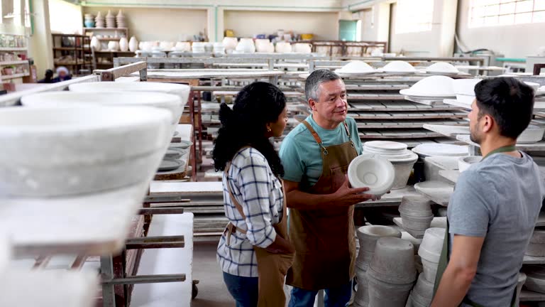 Mature supervisor at a pottery factory training diverse new hires explaining the process