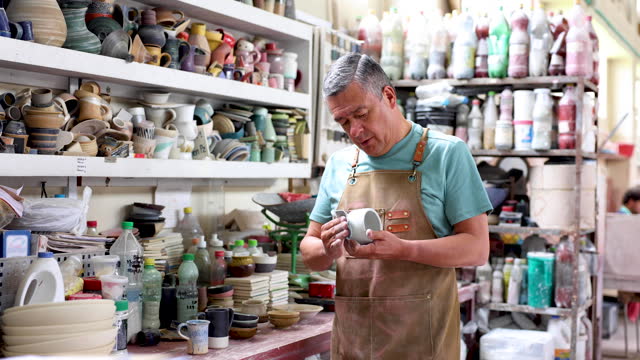 Focused mature man sanding a mug at a pottery factory