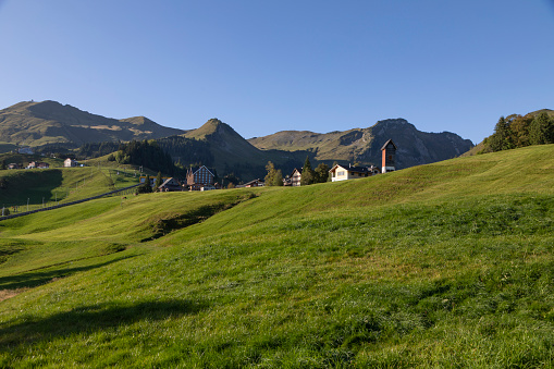 Eben im Pongau, Salzburg - Austria - 06-16-2021: A small chapel stands in an alpine meadow with a tractor in use, in the middle of the lush Austrian landscape