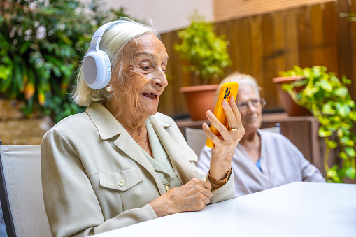 Elder woman listening to music with headphones and a mobile in a nursing home