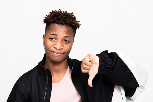 Afro american woman in bad mood standing on white background in studio showing dissatisfied emotions wearing stylish hairdress showing thumb down dislike situation.