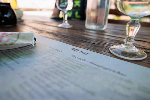 close up view in perspective, showing a wooden table, set for lunch, in summer, with view in particular on the menu paper