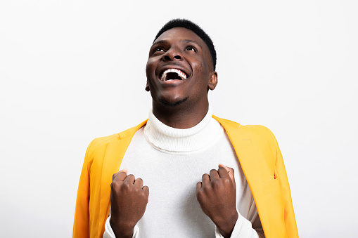 Portrait of cheerful contented young African American man over blue background sense of happiness portrait man clenching fists celebrating victory suggesting feeling of confidence and success.