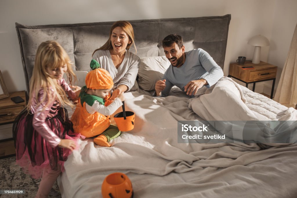 Halloween morning Little sisters in Halloween costumes jumping on parents bed and waking them up. Bed - Furniture Stock Photo