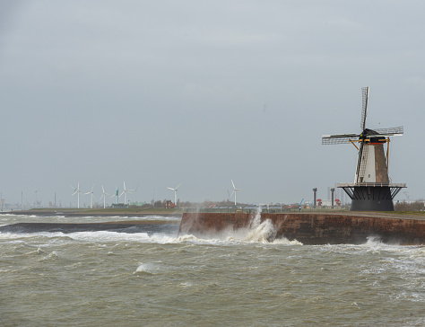 Windmills, new and old at the seashore during the storm with a wild sea.