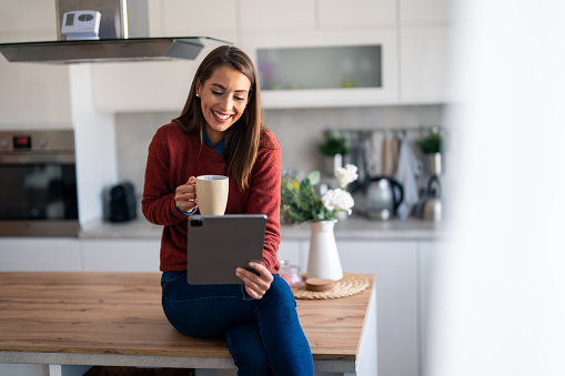 Young woman freelancer reading on digital tablet pc while drinking coffee at home.
