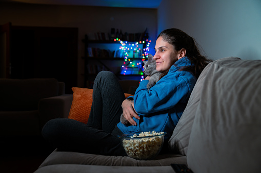Beautiful woman sitting on a couch and watching movie at night in the living room at home.