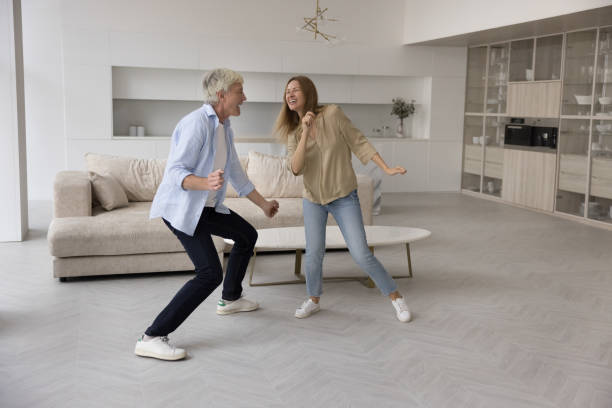 Excited active old retired dad and adult daughter enjoying movement Excited active old retired dad and active adult daughter woman enjoying movement, fitness activity at home, dancing to music in modern apartment interior, smiling, laughing teacher retirement party stock pictures, royalty-free photos & images