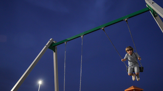 a child plays with the swing on the playground  in the night
