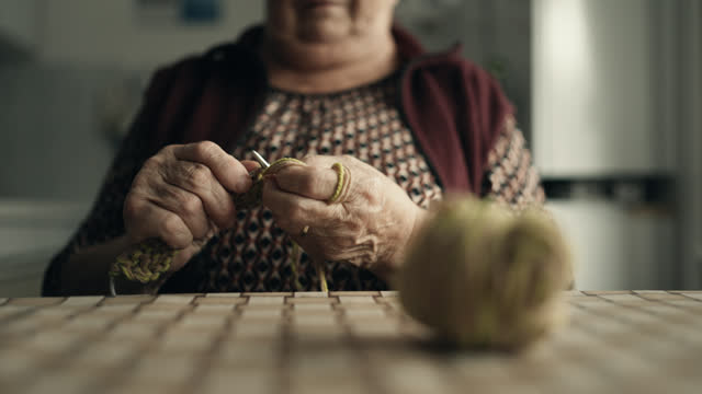 SLO MO Rack Focus view of Hands of Elderly Woman Knitting with Needles and Ball Of Wool on Table at Home