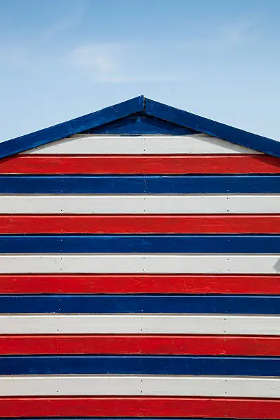 A traditional, beautiful painted beach hut, with red, white and blue horizontal stripes.