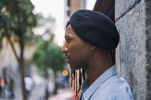 young African-American man sideways leaning against a wall wearing a sideways hat