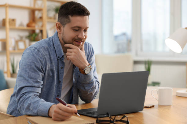 istock Happy man writing notes while working on laptop at wooden desk in room 1754748389