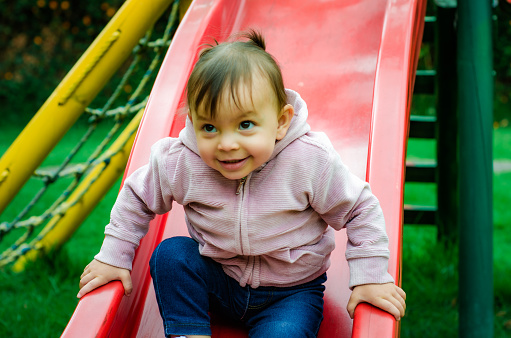 Baby Girl playing on outdoor playground. Kids play on school or kindergarten yard. Active kid on colorful slide. Little girl on outdoors