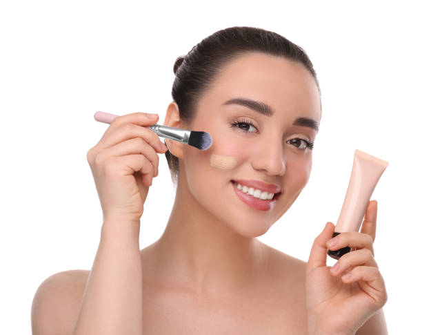 istock Woman with tube applying foundation on face using brush against white background 1754761047