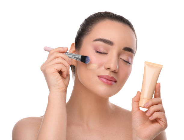 istock Woman with tube applying foundation on face using brush against white background 1754762796
