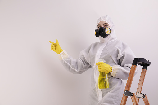 Woman in protective suit cleaning mold with sprayer on wall